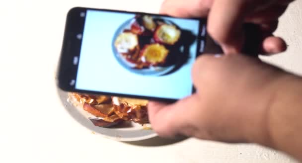 Joven fotografiando el almuerzo en el restaurante con el teléfono. Un joven tomando fotos de pasteles de comida en el teléfono inteligente, fotografiando comida con cámara móvil . — Vídeos de Stock