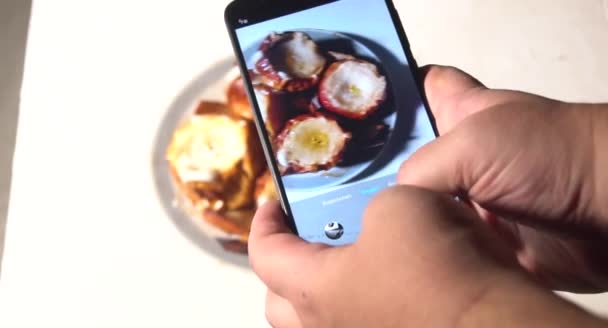 若い男が電話でレストランで昼食を撮っている。スマホでケーキの食べ物を写真に撮り、携帯カメラで食事を撮る青年. — ストック動画