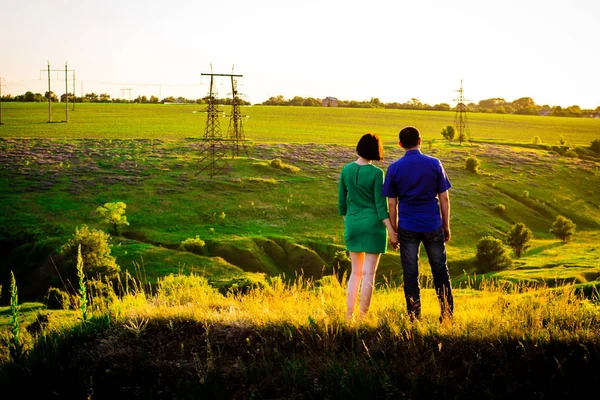 Lány és fiú fogják egymás kezét, és egy zöld dombon állnak. Napnyugta. Visszanézés. — Stock Fotó