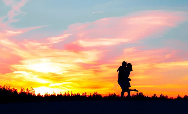 Sylwetka dziewczyny zbliża się do ukochanego chłopaka i przytula go na tle zachodu słońca i kóz. — Zdjęcie stockowe