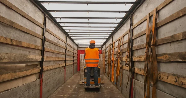 Forklift yükleyicisiyle karton kutular yükleyen üniformalı bir depo çalışanı.