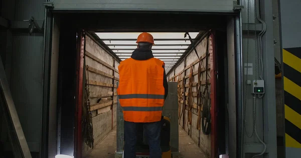 Forklift yükleyicisiyle karton kutular yükleyen üniformalı bir depo çalışanı.