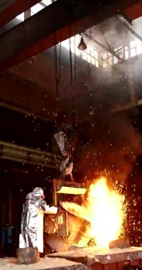 Telefonlar ve tabletler için dikey video. Metalurjik bir fabrikada portakal metali eritmek. Kepçeden sıvı demir.