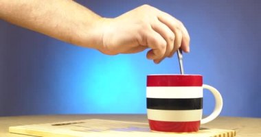 Erkek eli, şekeri şeffaf bir bardakta çay ile karıştırır.