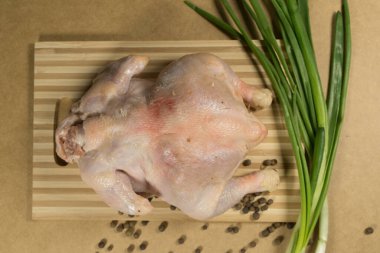 Çiğ tavuk leşi, tavuk. Soğan, limon, mantar, sarımsak, biberiyeli çiğ tavuk leşi, baharat ve otlar ahşap bir masada, gri bir arka planda.