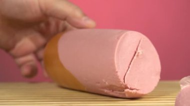 Mutfaktaki ahşap bir kesme tahtasının üzerinde jambon dilimleyen bir adamın ellerini yakın plan çek.
