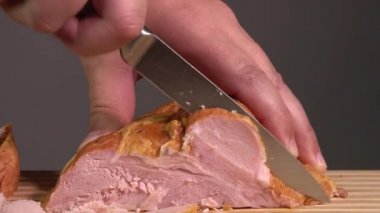 Mutfaktaki ahşap bir kesme tahtasının üzerinde jambon dilimleyen bir adamın ellerini yakın plan çek.