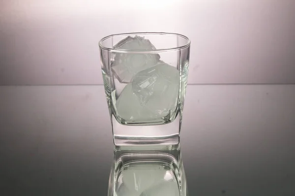 Glass of whiskey with ice cubes in mirror image. Horizontal image with copy space. Gray background