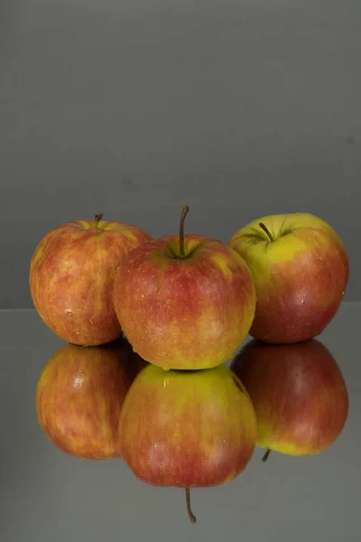 Three red apples on mirroring table on mirror gray background with reflection isolated close up. Mirror background