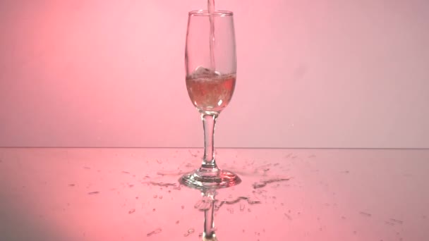 慢慢地把红酒从瓶子倒入酒杯中 红葡萄酒的特写在玻璃杯中形成美丽的波浪 粉红背景下倒入酒杯的葡萄酒 镜像反射 — 图库视频影像