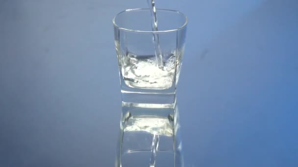 ウォッカをボトルからゴブレットに注ぐ動きが遅い 青い背景にガラスに注ぐウォッカ 鏡面反射 — ストック動画