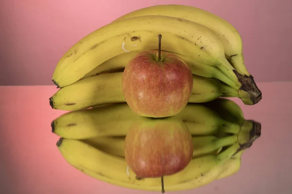 A bunch of bananas and apples on mirroring table on mirror red background with reflection isolated close up. Mirror background