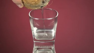 Hindistan cevizi suyu bardağa dökülür. Kırmızı ayna arka planında