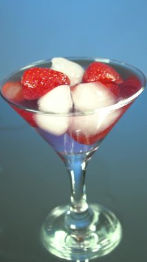 Bir bardak buz ve çileğe tekila dökmek, yavaş çekim, ayna arka plan. Akıllı telefonlar ve tabletler için dikey video