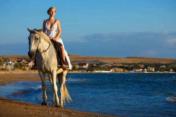 beautiful girl on a white horse on background of the sea, in a dress of Amazon . Holiday and vacation concept