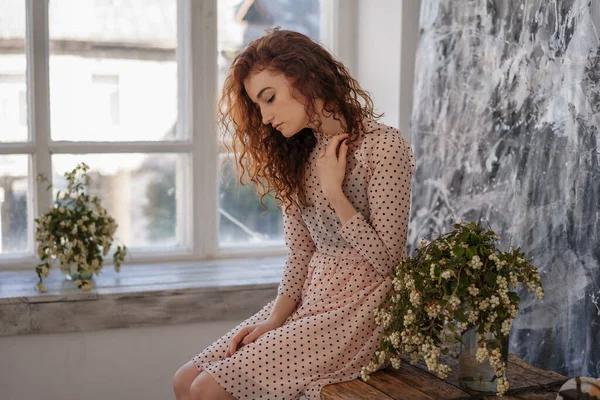 A single woman with red hair sits on the background of a window, the concept of loneliness