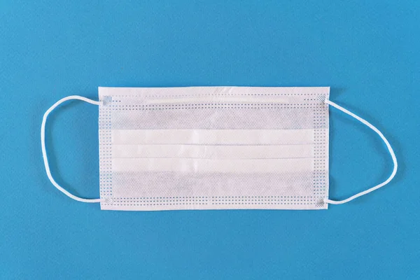 Surgical mask with rubber ear straps. Procedure mask from bacteria. Protection concept. On a blue background