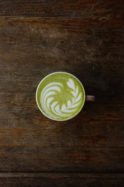 Bir fincan yeşil çay, ahşap arka planda matcha latte.