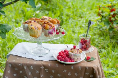 Camdan pasta tezgahında ahududu olan kekler beyaz peçetenin üstünde ve yeşil arka planda ahududu olan bir tabak.