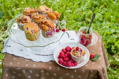 Camdan pasta tezgahında ahududu olan kekler beyaz peçetenin üstünde ve yeşil arka planda ahududu olan bir tabak.