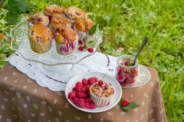 Camdan pasta tezgahında ahududu olan kekler beyaz peçetenin üstünde ve yeşil arka planda ahududu olan bir tabak.
