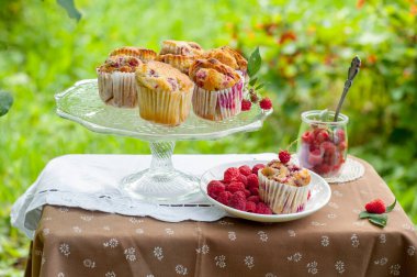 Camdan pasta tezgahında ahududu olan kekler beyaz peçetenin üstünde ve yeşil arka planda ahududu olan bir tabak.