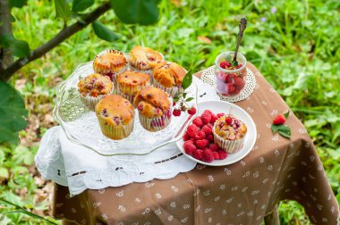 Camdan pasta tezgahında ahududu olan kekler beyaz peçetenin üstünde ve yeşil arka planda ahududu olan bir tabak.