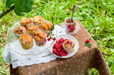 Camdan pasta tezgahında ahududu olan kekler beyaz peçetenin üstünde ve yeşil arka planda ahududu olan bir tabak.
