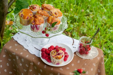 Camdan pasta tezgahında ahududu olan kekler beyaz peçetenin üstünde ve yeşil arka planda ahududu olan bir tabak.