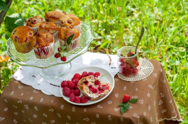 Camdan pasta tezgahında ahududu olan kekler beyaz peçetenin üstünde ve yeşil arka planda ahududu olan bir tabak.