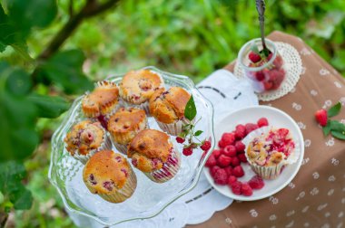 Camdan pasta tezgahında ahududu olan kekler beyaz peçetenin üstünde ve yeşil arka planda ahududu olan bir tabak.