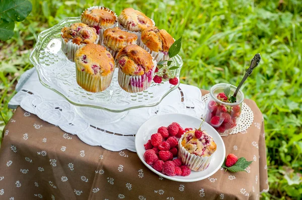 Camdan pasta tezgahında ahududu olan kekler beyaz peçetenin üstünde ve yeşil arka planda ahududu olan bir tabak.