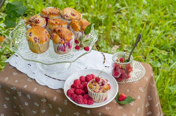 Camdan pasta tezgahında ahududu olan kekler beyaz peçetenin üstünde ve yeşil arka planda ahududu olan bir tabak.