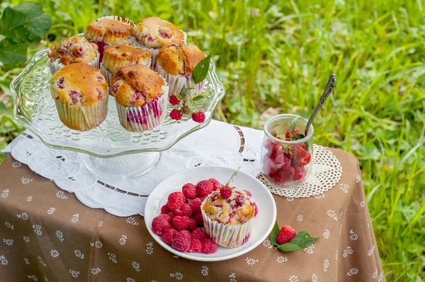 Camdan pasta tezgahında ahududu olan kekler beyaz peçetenin üstünde ve yeşil arka planda ahududu olan bir tabak.