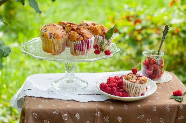 Camdan pasta tezgahında ahududu olan kekler beyaz peçetenin üstünde ve yeşil arka planda ahududu olan bir tabak.