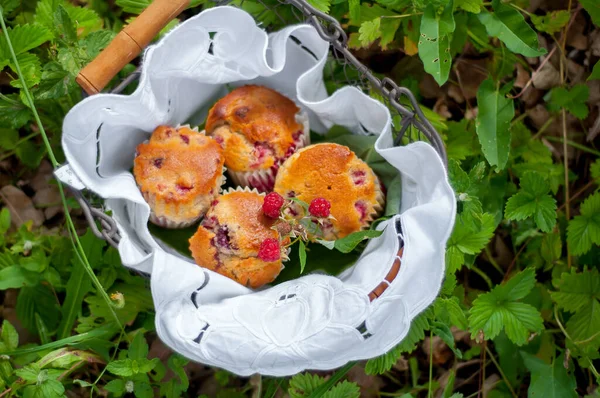 Bahçedeki yeşil çimlerin üzerinde beyaz bir peçete üzerinde sepetin içinde ahududu kekleri.