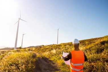 Sert şapkalı genç mühendis gün batımında yel değirmenleriyle çalışıyor.