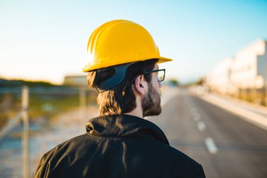 Şapkalı genç adam inşaatta çalışıyor. Kentsel arkaplan üzerine plan üzerinde çalışan mimar.