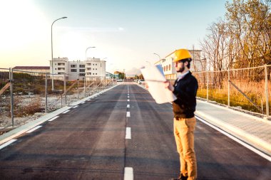 Şapkalı genç adam inşaatta çalışıyor. Kentsel arkaplan üzerine plan üzerinde çalışan mimar.