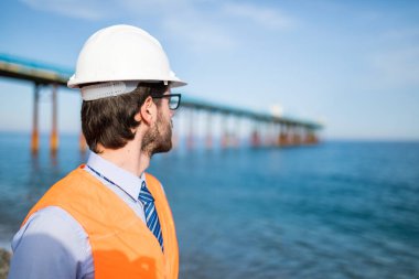 Şapkalı genç adam inşaatta çalışıyor. Deniz kenarında köprü tadilatında çalışan mimar.