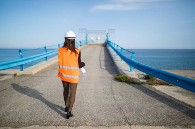 Şapkalı genç bir kadın inşaatta çalışıyor. Deniz kenarında köprü tadilatında çalışan mimar.