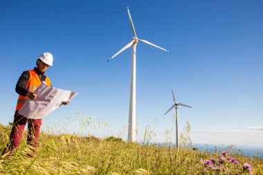 Sert şapkalı genç mühendis gün batımında yel değirmenleriyle çalışıyor.