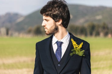 Üzerinde sarı mimoza çiçekleri olan takım elbiseli bir adamın portresi bulanık doğal arka planda.