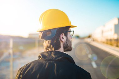 Şapkalı genç adam inşaatta çalışıyor. Kentsel arkaplan üzerine plan üzerinde çalışan mimar.