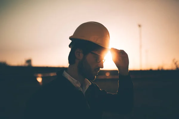 Young man in hard hat working on construction. Architect working with blueprint on urban background.