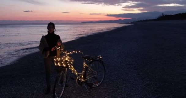 Mujer Disfrutando Puesta Sol Junto Mar Con Guirnalda Bicicleta — Vídeos de Stock