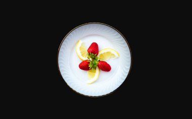 Beyaz tabakta limon parçaları olan çilekler.