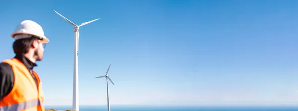 Miğferli işçi, değirmenlerle sahada duruyor.