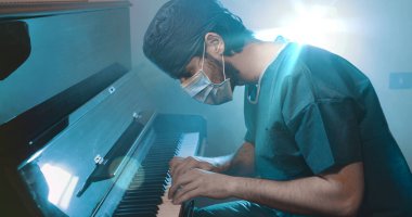 Üniformalı ve maskeli bir doktor piyano çalıyor. 