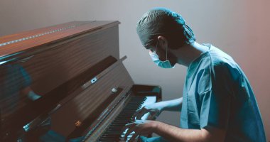 Üniformalı ve maskeli bir doktor piyano çalıyor. 